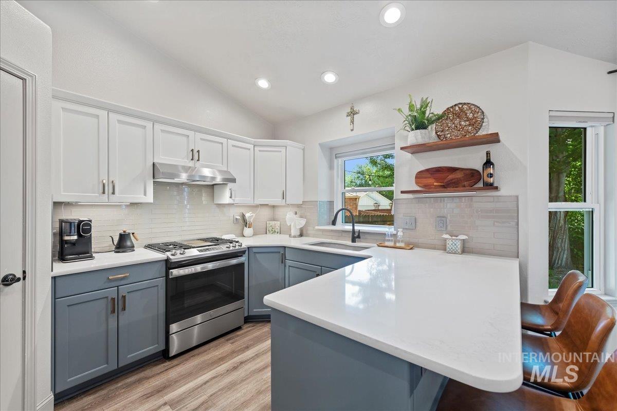 Kitchen featuring stainless steel gas stove, open shelves, gray cabinetry, a peninsula, and under cabinet range hood