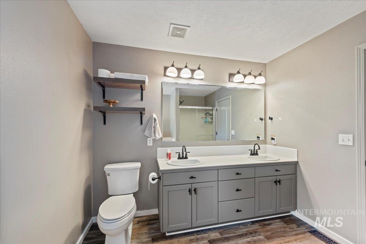 Bathroom with wood finished floors, double vanity, an enclosed shower, and a textured ceiling