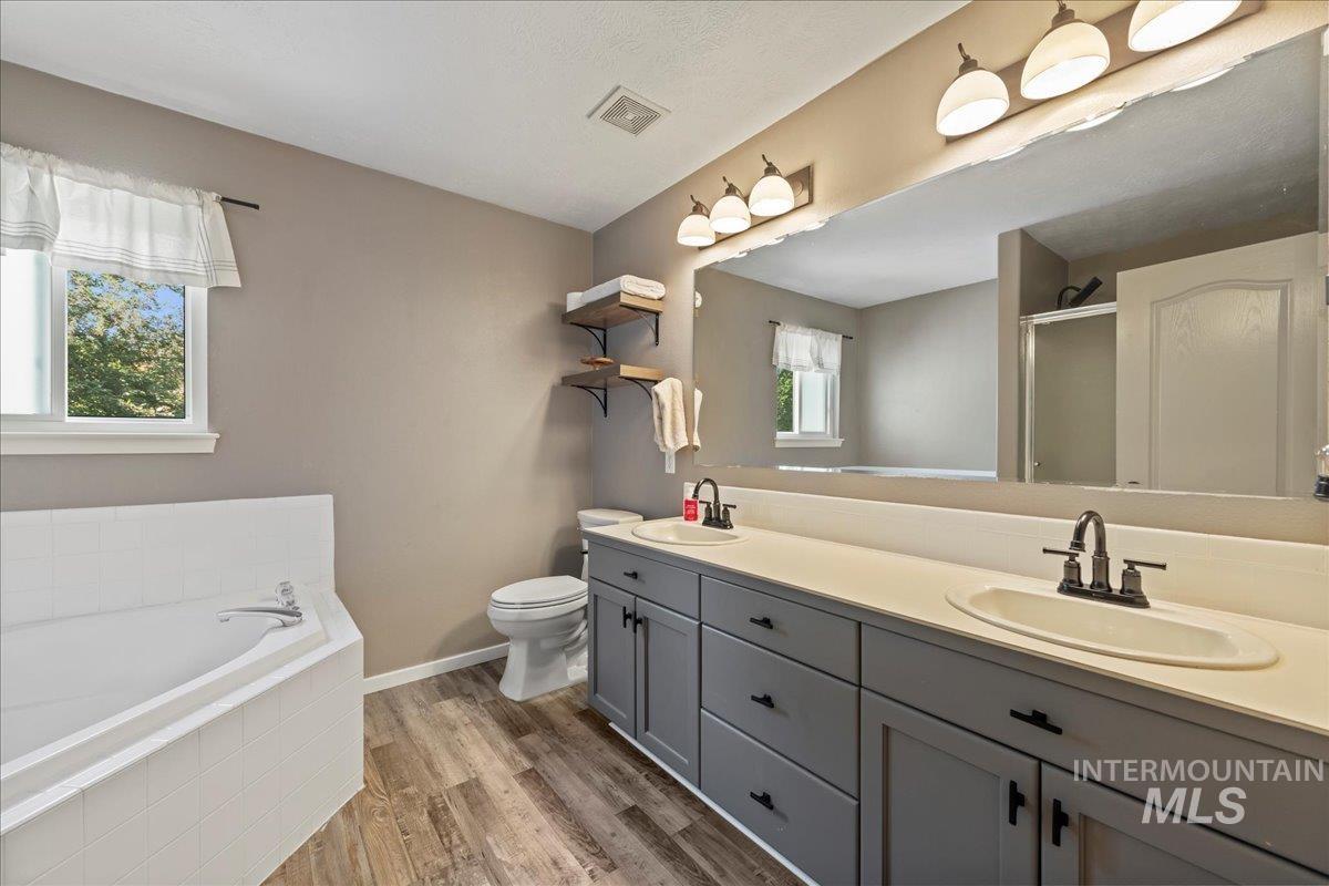 Bathroom with double vanity, a bath, wood finished floors, and a stall shower