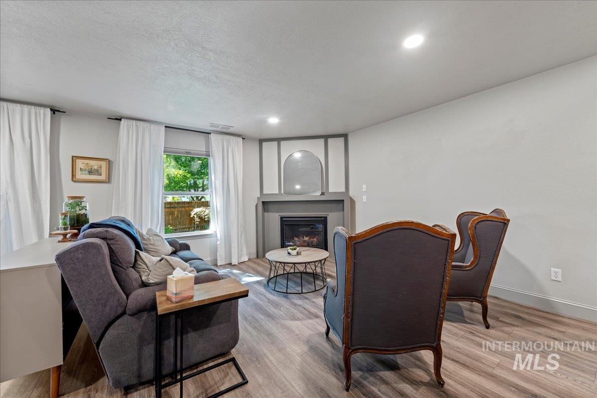 Living room with light wood-type flooring, a glass covered fireplace, recessed lighting, and a textured ceiling