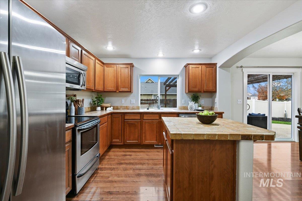 Kitchen featuring appliances with stainless steel finishes, a center island, brown cabinets, dark wood finished floors, and healthy amount of natural light