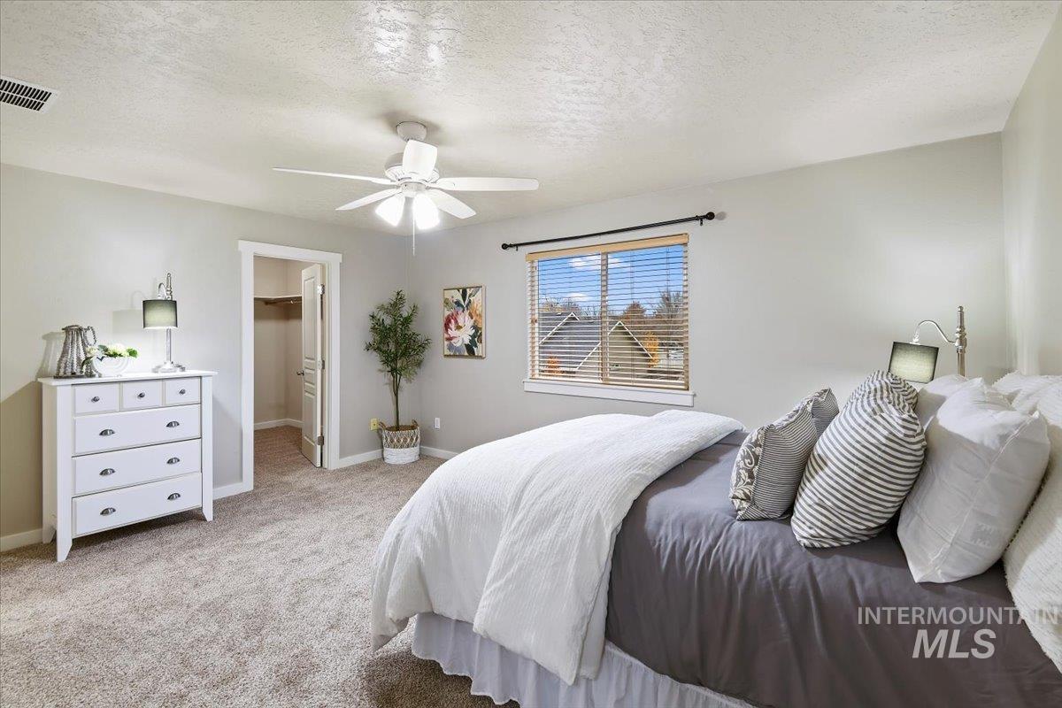 Bedroom with a spacious closet, a textured ceiling, light carpet, and a ceiling fan