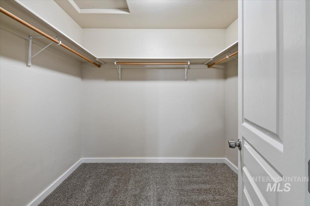 Walk in closet with dark carpet and attic access