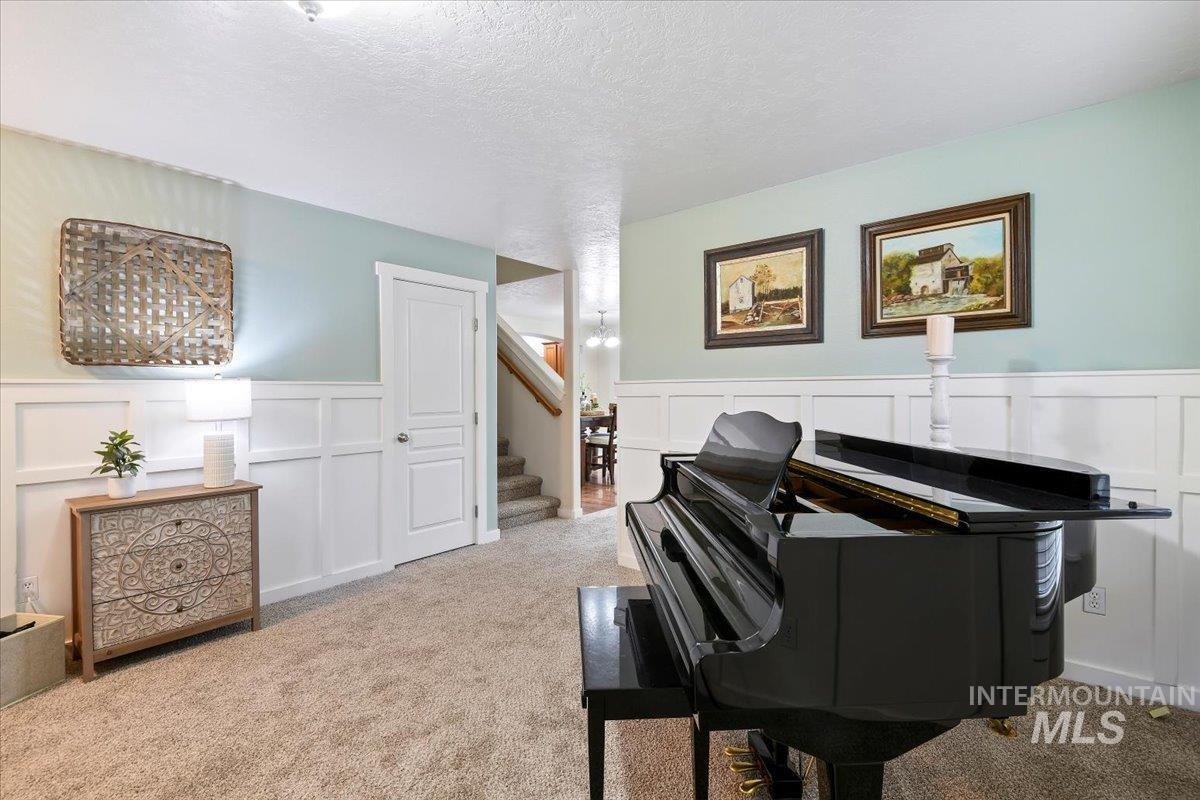 Sitting room with a decorative wall, a wainscoted wall, a textured ceiling, carpet flooring, and stairway