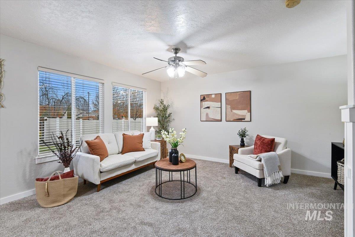 Living area featuring a textured ceiling, light carpet, a ceiling fan, and a fireplace