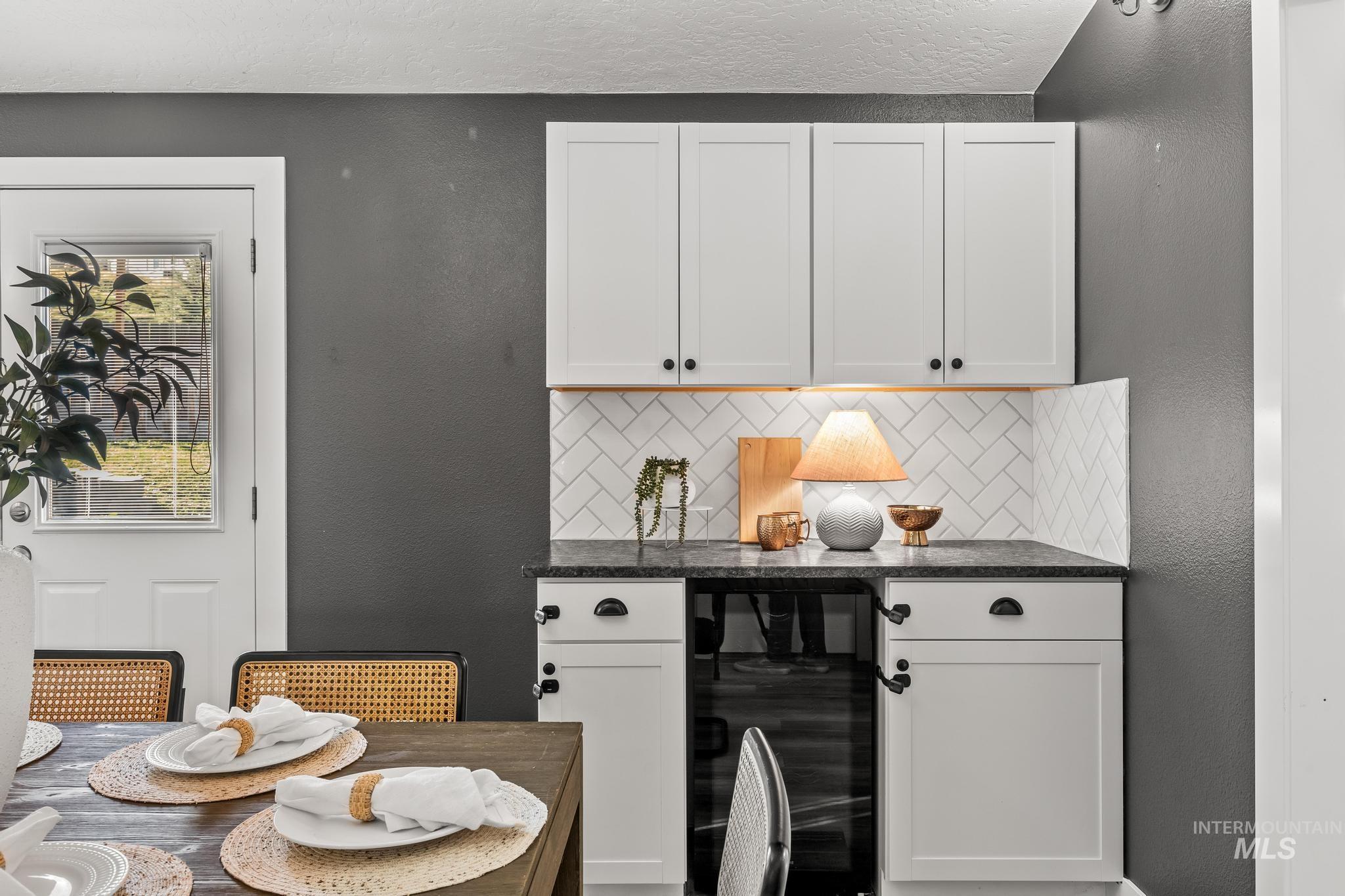 Kitchen with a textured wall, beverage cooler, white cabinetry, tasteful backsplash, and dark stone countertops