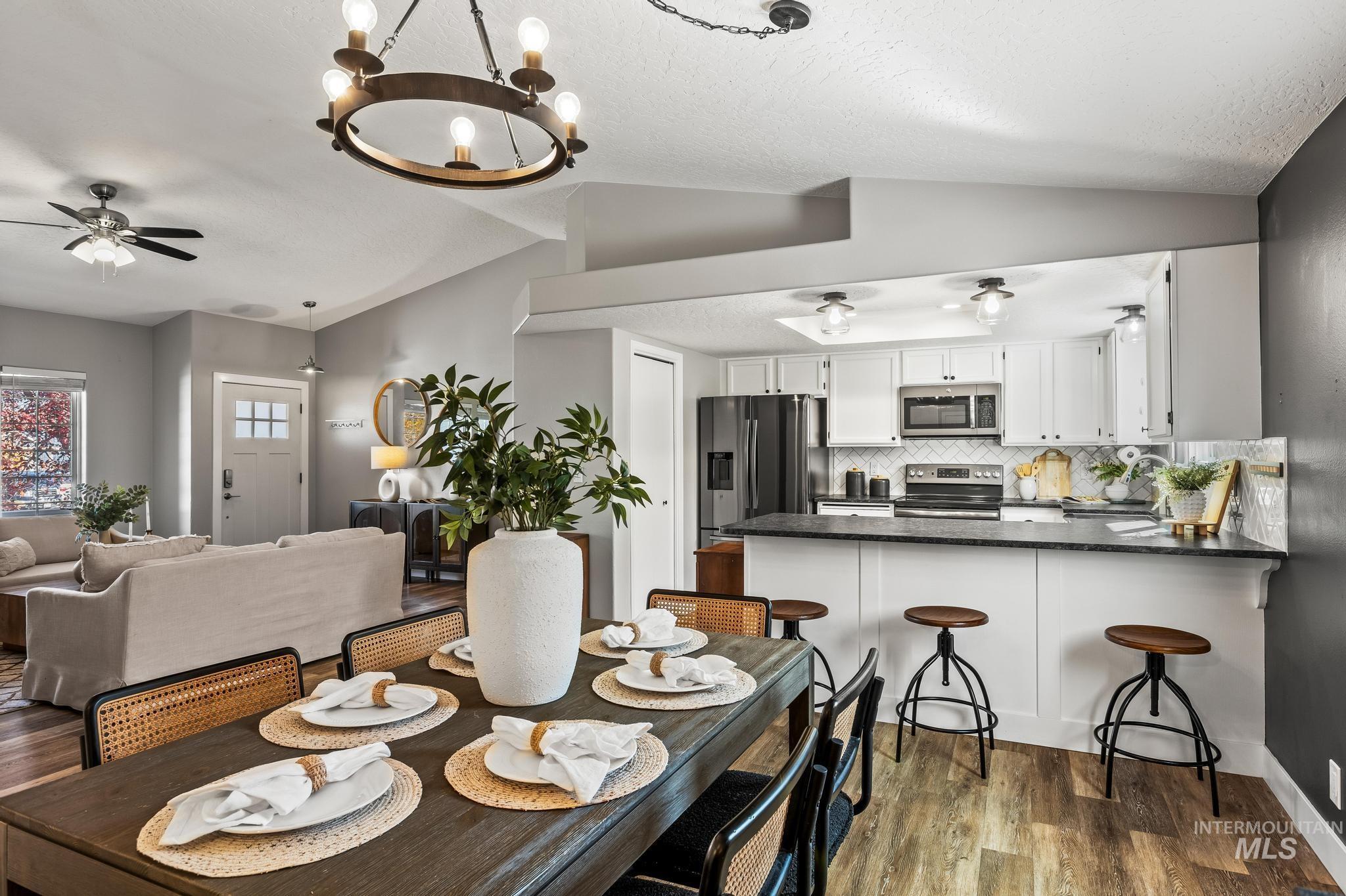 Dining room featuring lofted ceiling, a ceiling fan, dark wood finished floors, a chandelier, and a textured ceiling