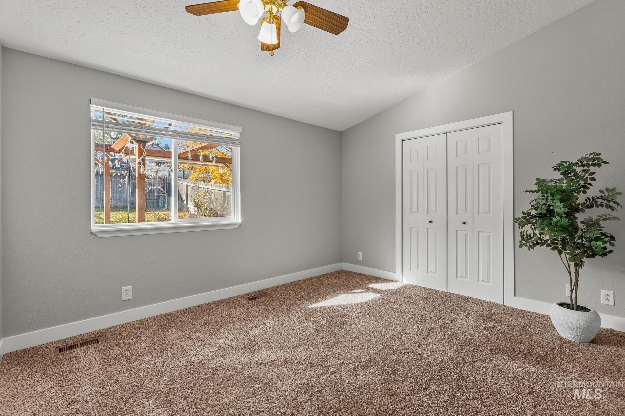 Unfurnished bedroom featuring a textured ceiling, lofted ceiling, carpet flooring, a closet, and ceiling fan