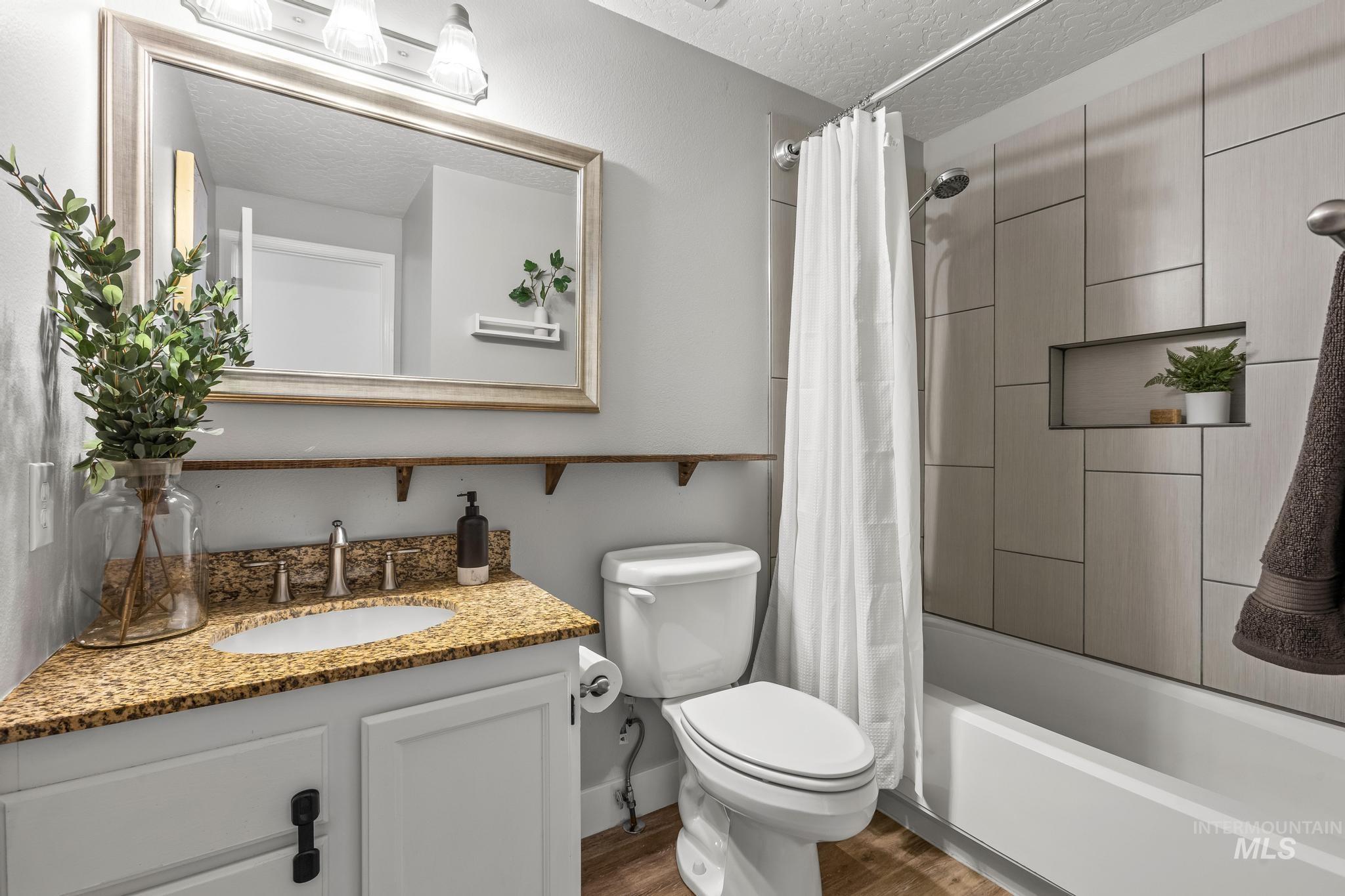 Bathroom featuring a textured ceiling, shower / tub combo, vanity, and dark wood-style floors