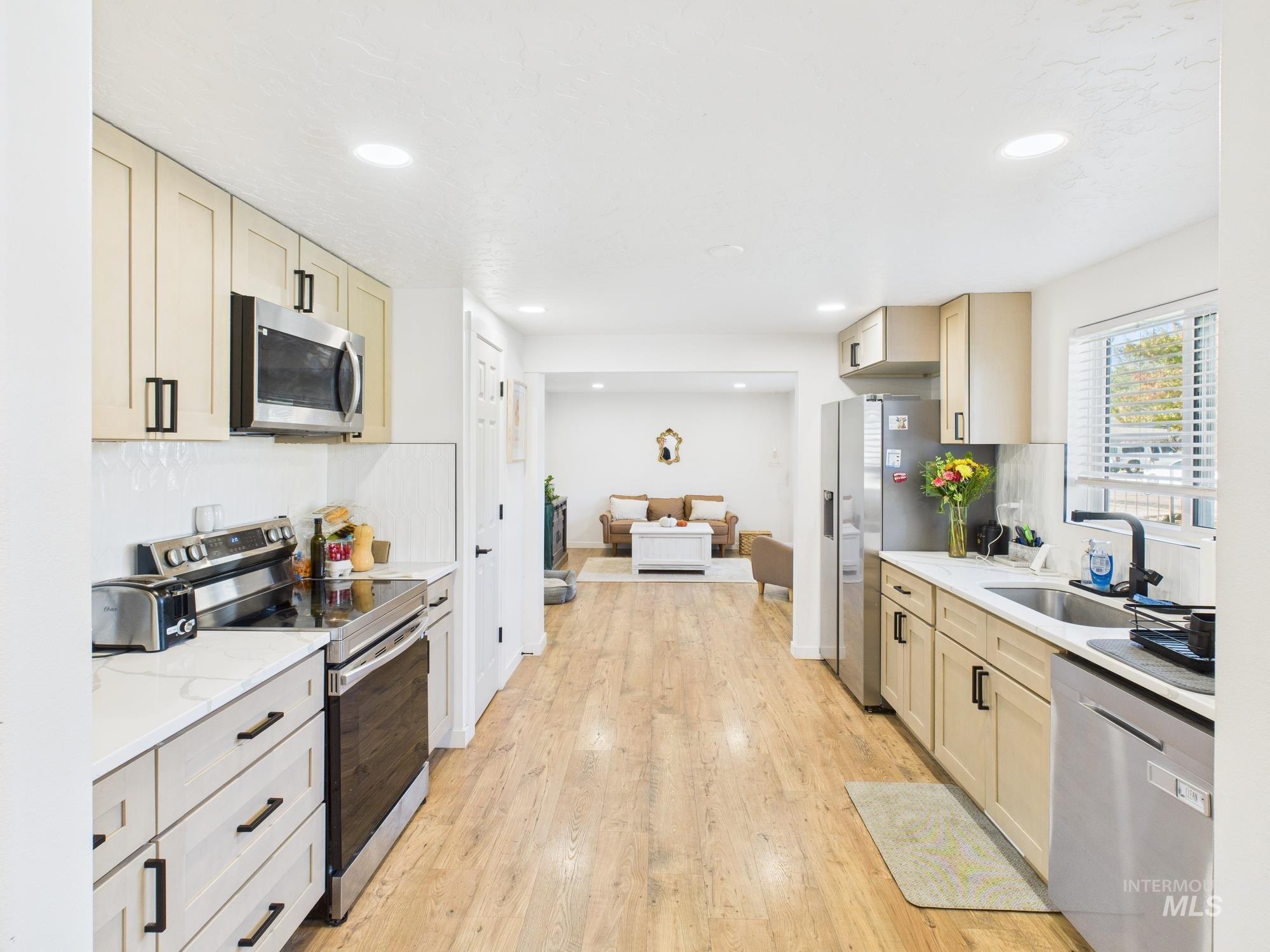 Kitchen with appliances with stainless steel finishes, light wood finished floors, open floor plan, recessed lighting, and light stone countertops