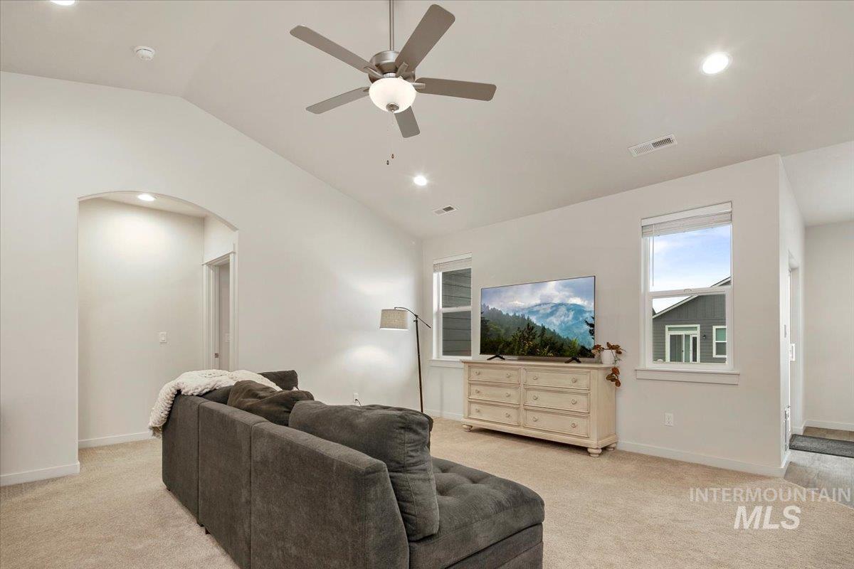 Living area with light carpet, vaulted ceiling, arched walkways, recessed lighting, and ceiling fan