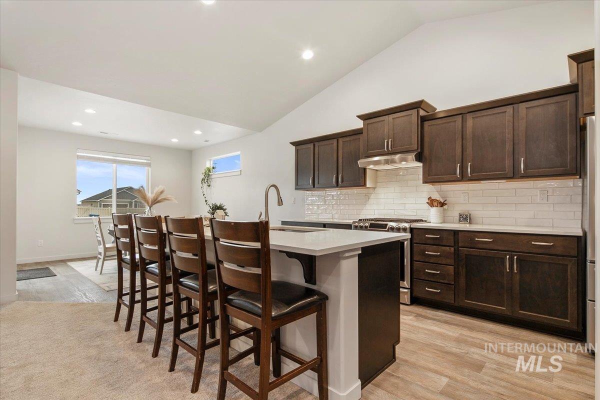 Kitchen with recessed lighting, dark brown cabinetry, stainless steel range with gas cooktop, lofted ceiling, and a kitchen bar