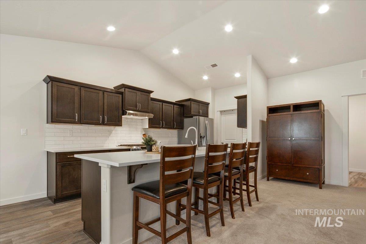 Kitchen featuring dark brown cabinetry, an island with sink, a breakfast bar area, tasteful backsplash, and lofted ceiling