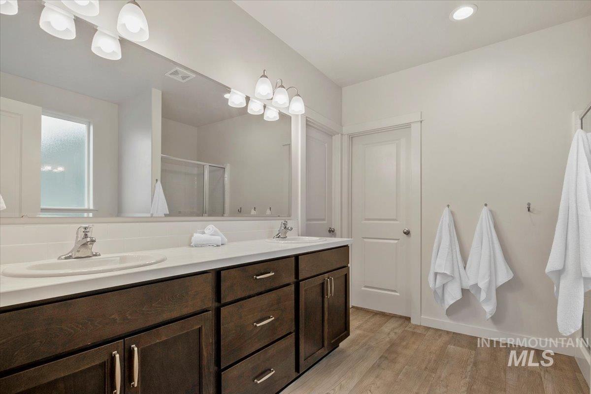 Bathroom featuring light wood-style flooring, double vanity, a shower stall, and recessed lighting