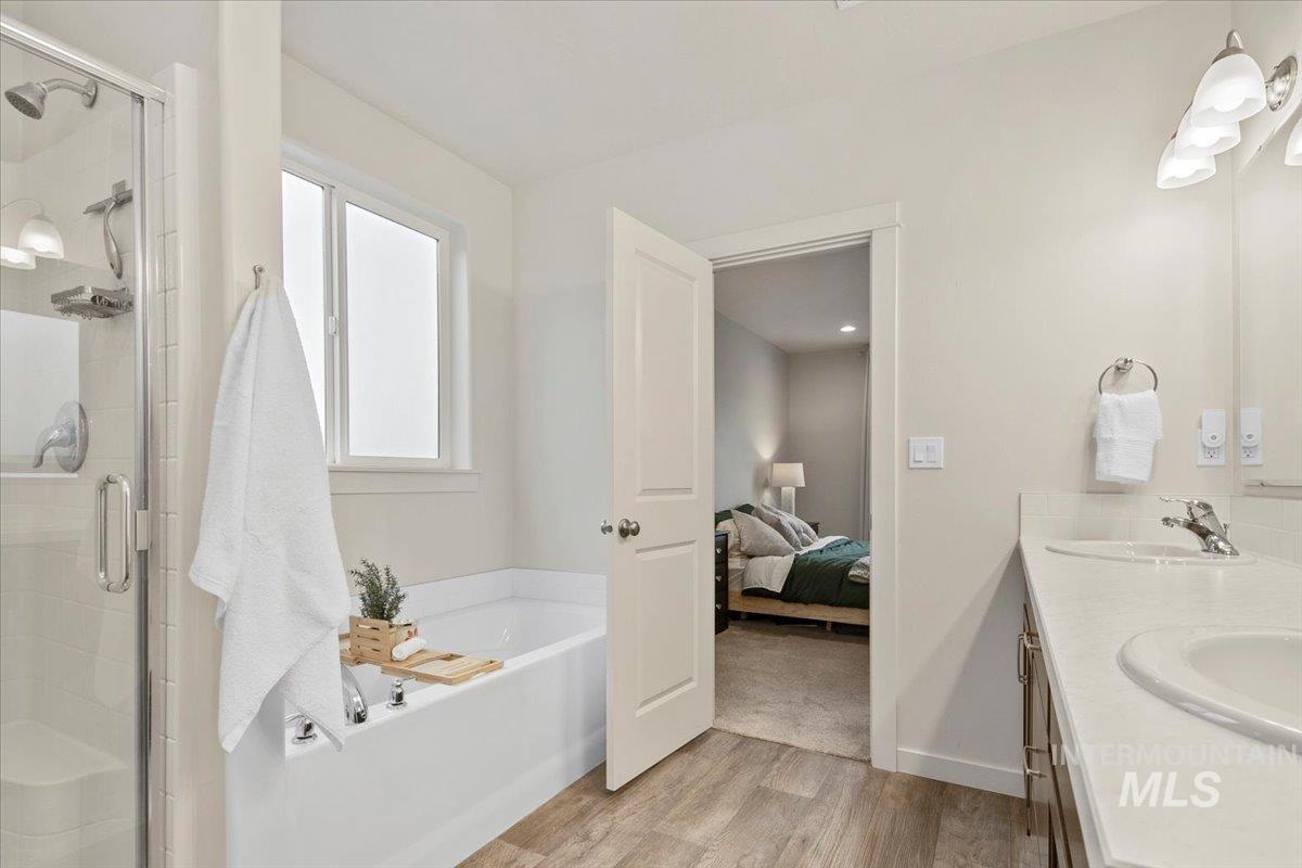 Bathroom with connected bathroom, light wood finished floors, a bath, double vanity, and a stall shower