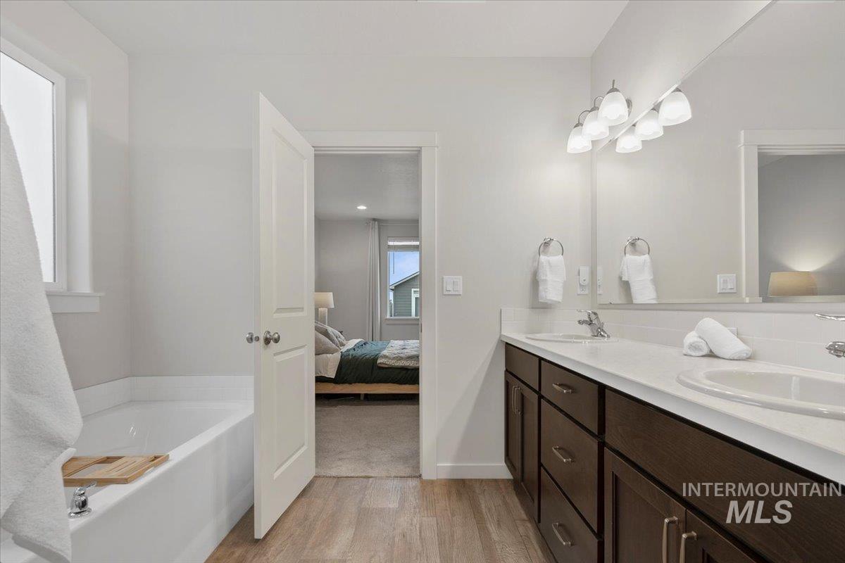 Ensuite bathroom with double vanity, light wood-type flooring, and a garden tub