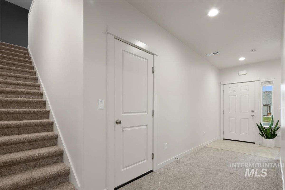 Foyer entrance with light colored carpet, recessed lighting, and stairway