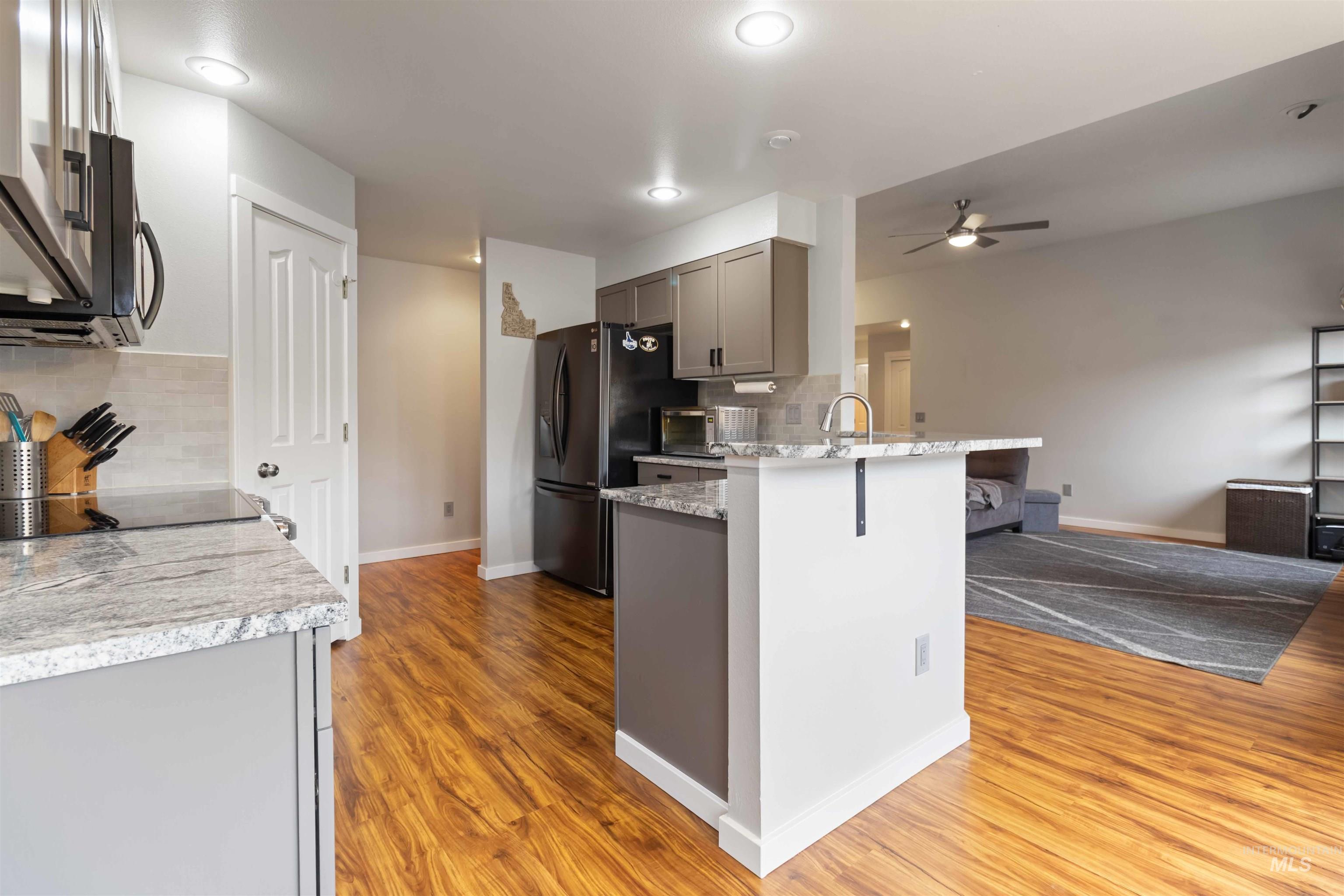 Kitchen with backsplash, gray cabinets, light stone counters, stainless steel microwave, and light wood-style flooring