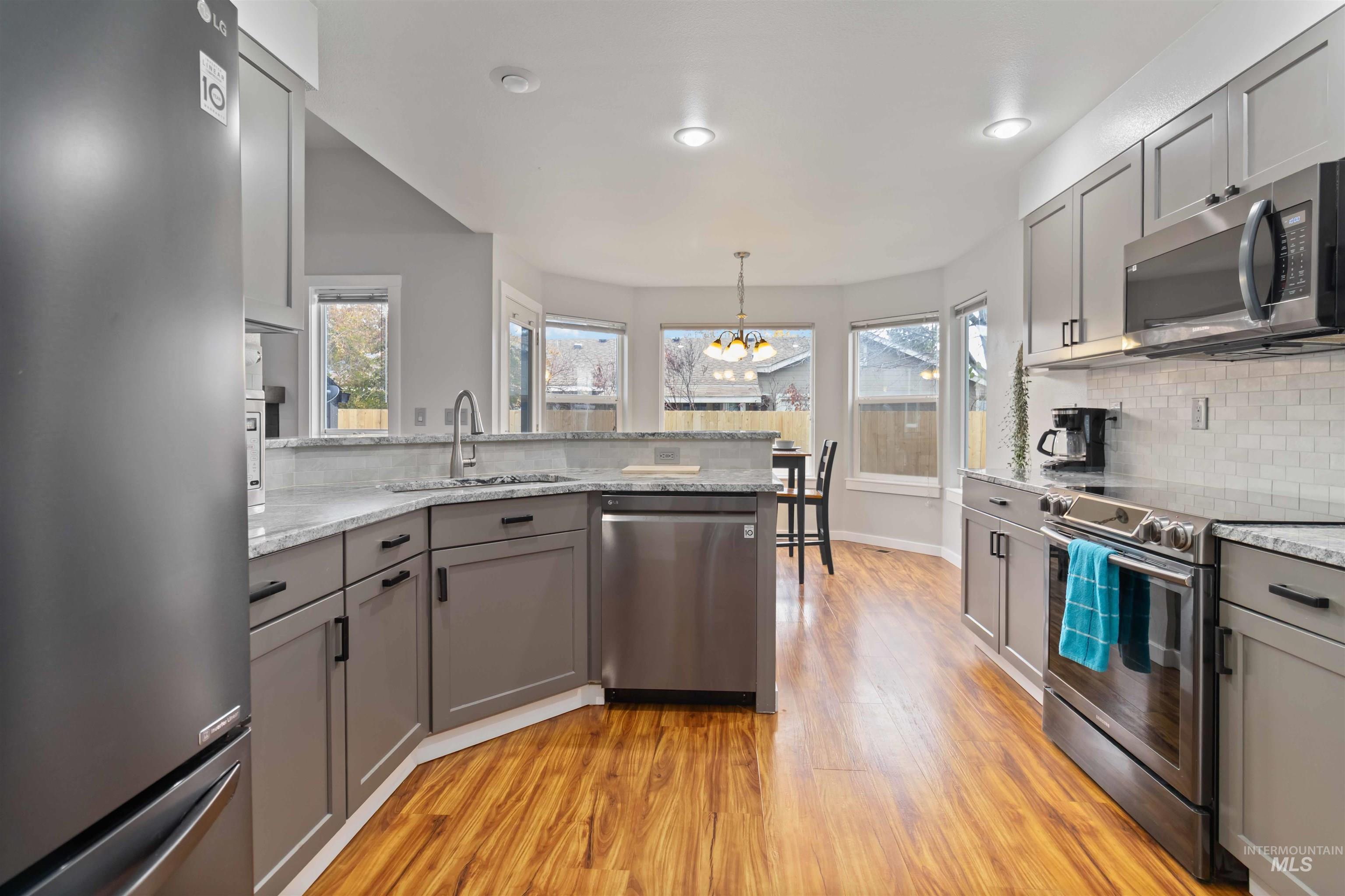 Kitchen featuring gray cabinetry, appliances with stainless steel finishes, decorative backsplash, and a chandelier