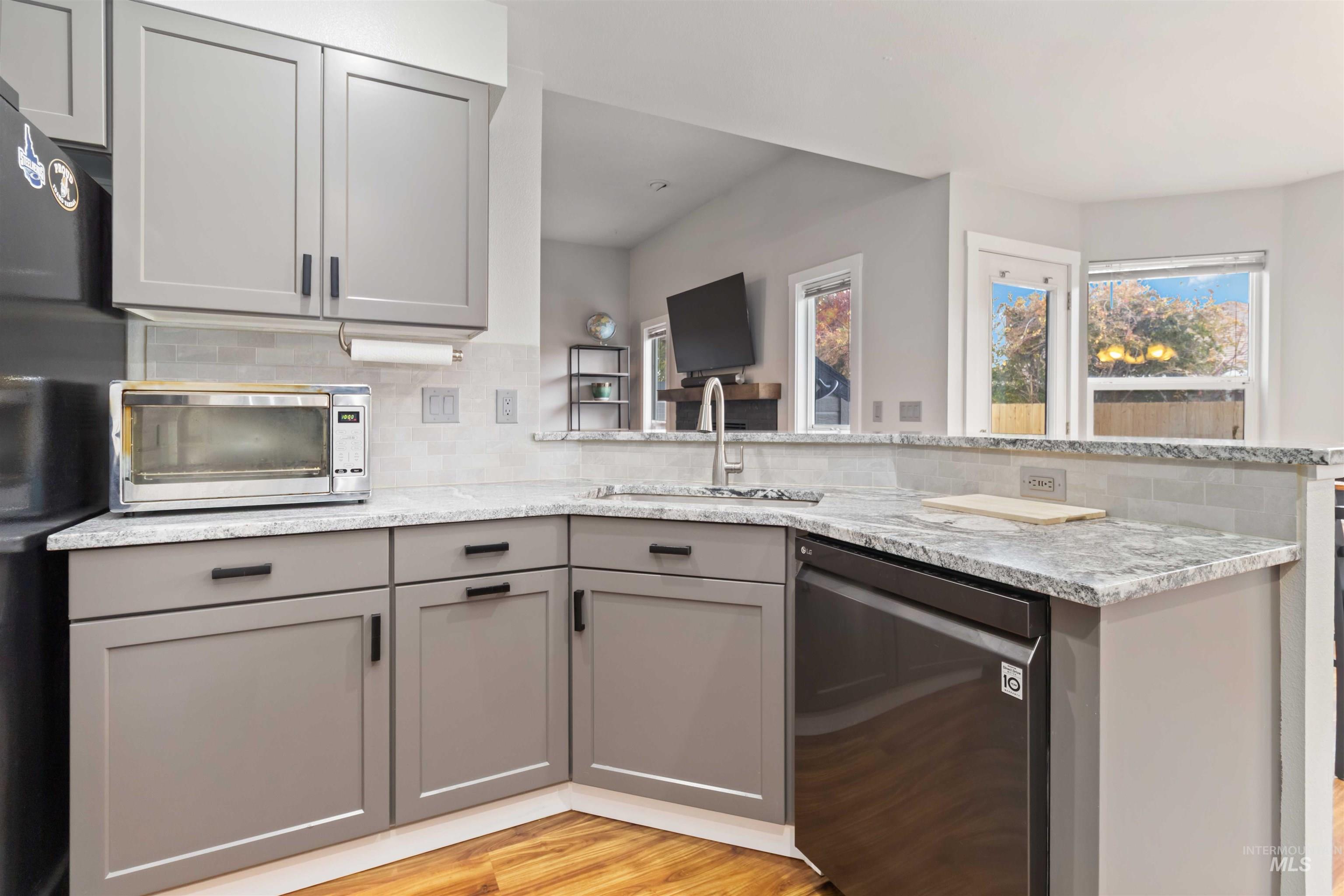 Kitchen featuring gray cabinetry, dishwasher, tasteful backsplash, freestanding refrigerator, and light stone counters