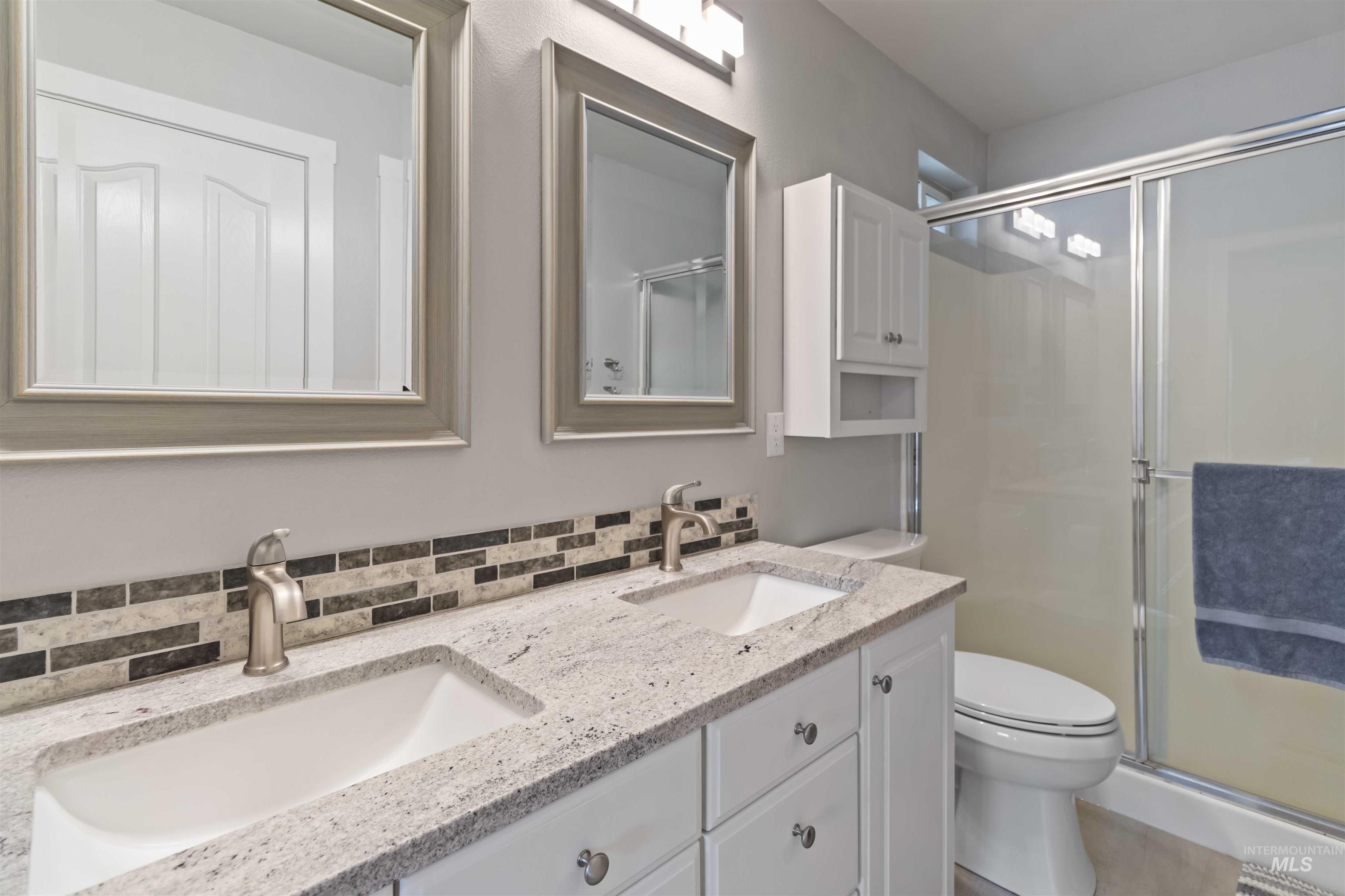 Bathroom featuring double vanity, a shower stall, and decorative backsplash