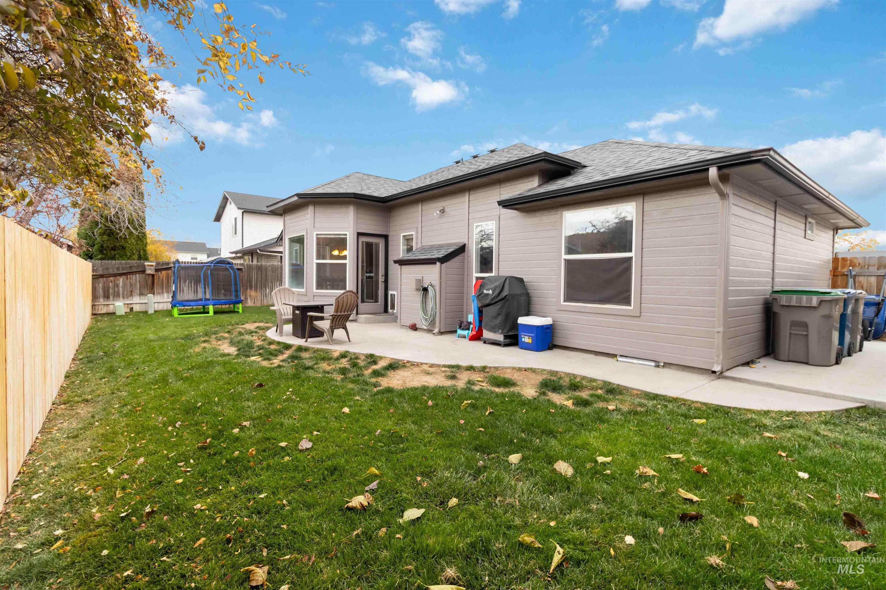 Back of house featuring a trampoline, a fenced backyard, a shingled roof, and a patio