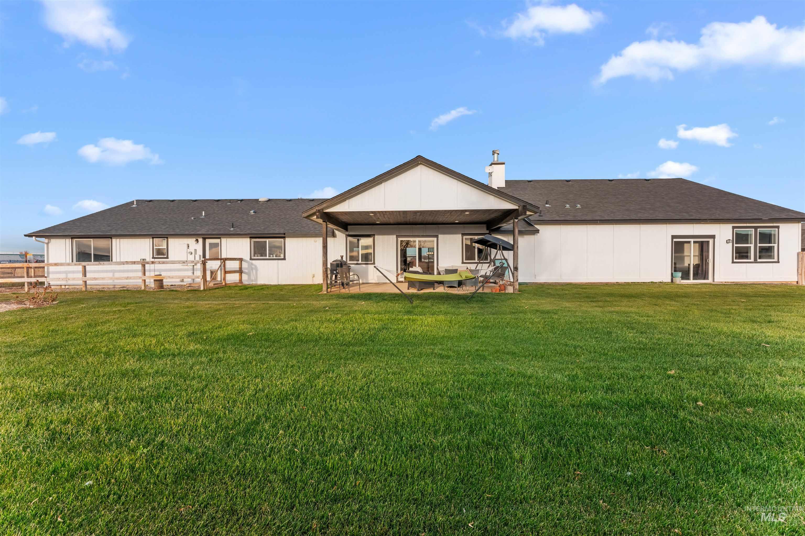 Rear view of property featuring a chimney, a patio, a yard, and roof with shingles