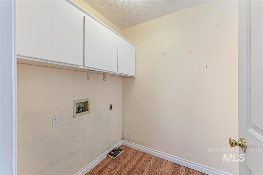 Laundry room with wood finished floors, a textured ceiling, cabinet space, hookup for an electric dryer, and washer hookup