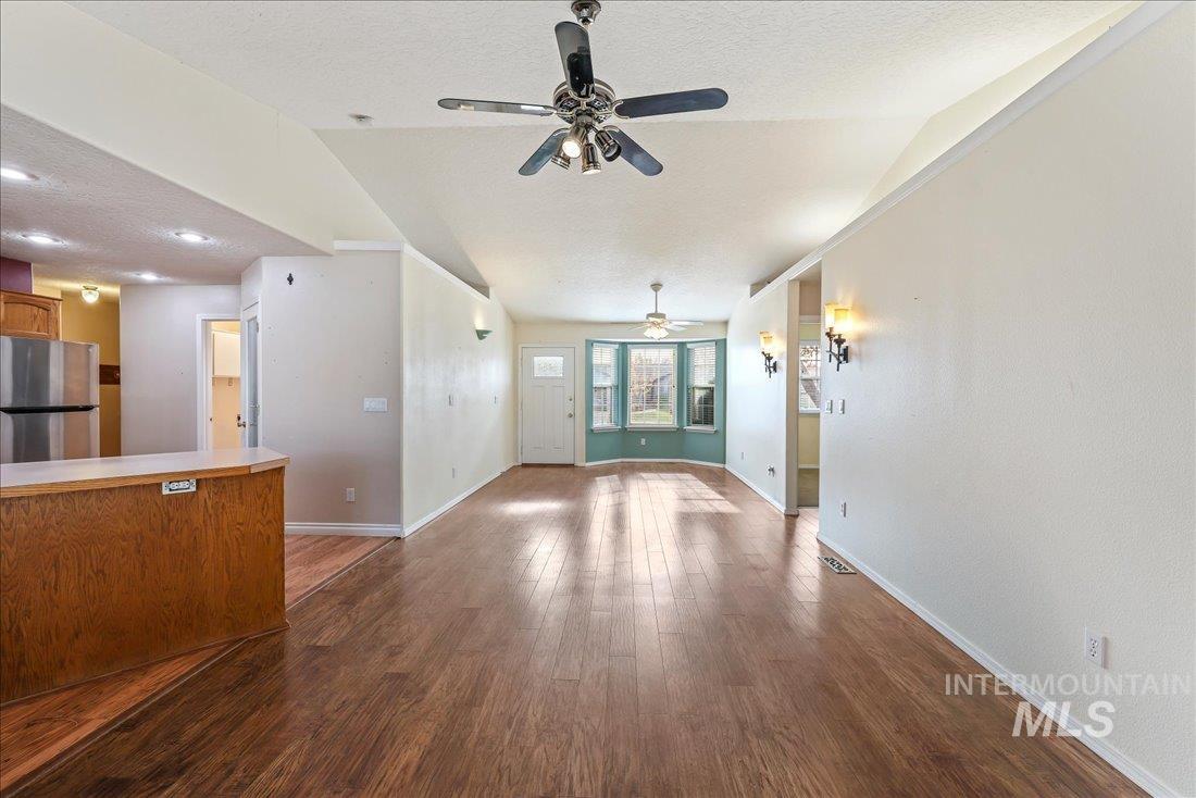 Unfurnished living room with a textured ceiling, dark wood finished floors, ceiling fan, and lofted ceiling