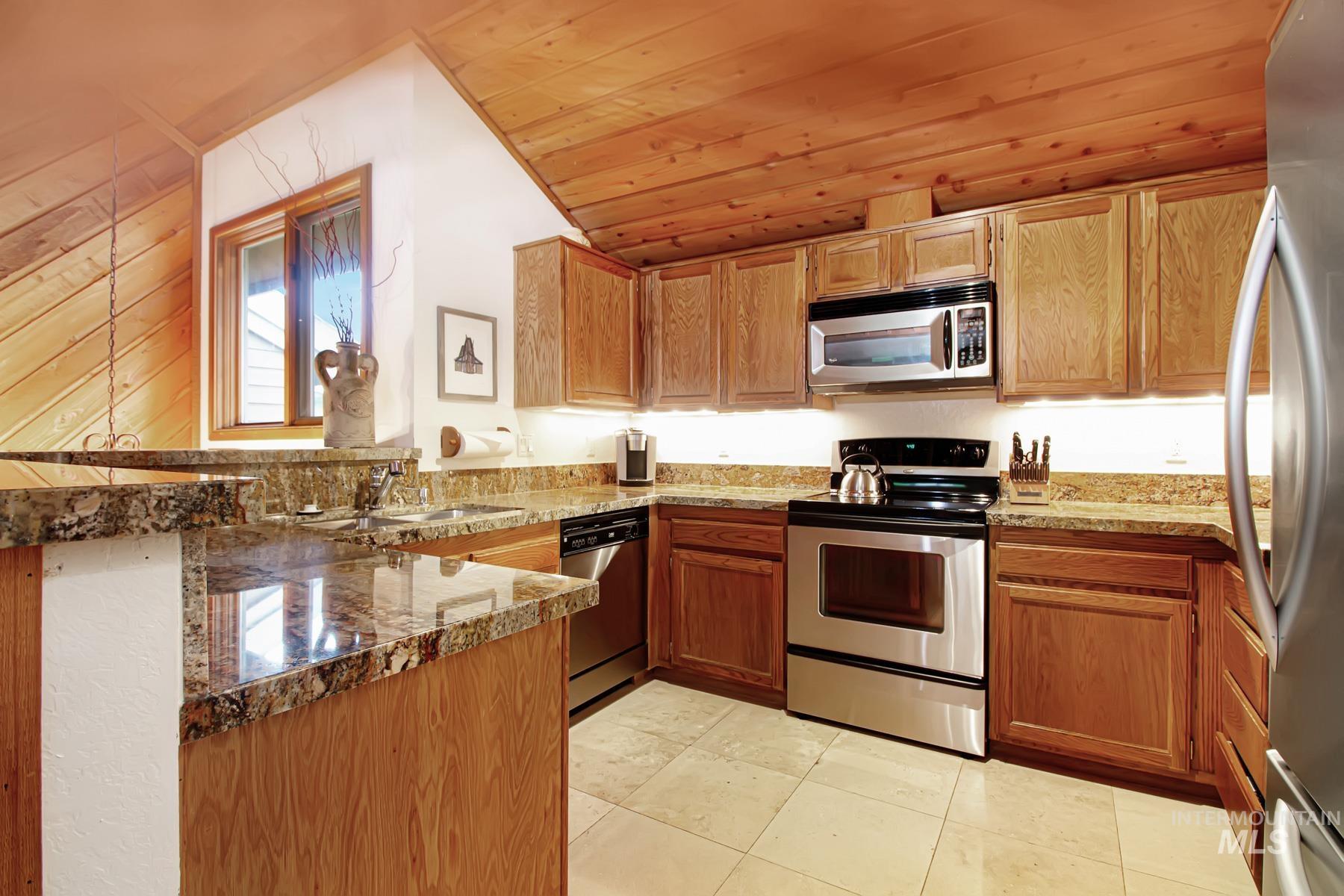 Kitchen with appliances with stainless steel finishes, a peninsula, wood ceiling, light tile patterned floors, and stone counters