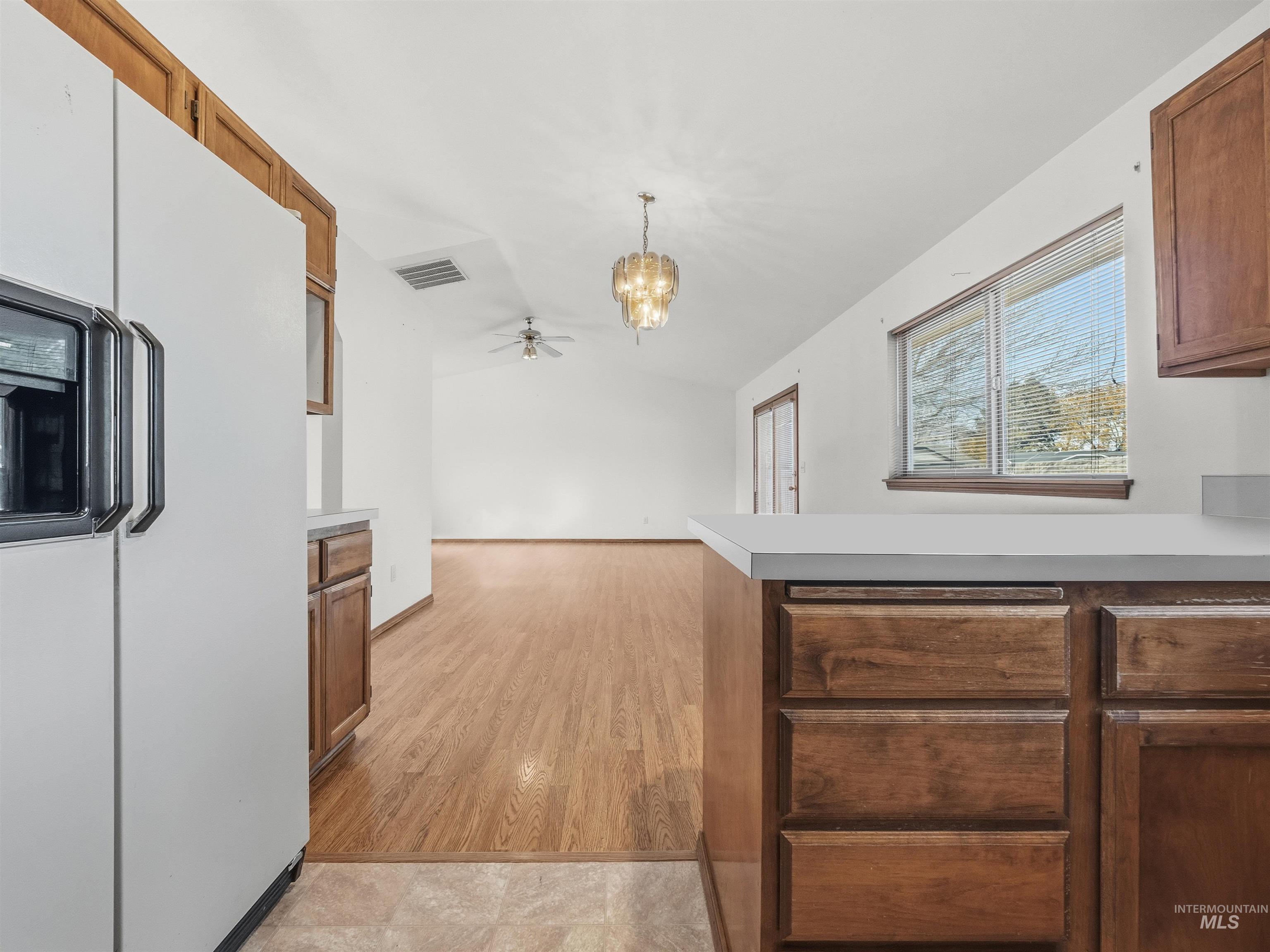 Kitchen featuring white refrigerator with ice dispenser, brown cabinetry, light countertops, vaulted ceiling, and ceiling fan