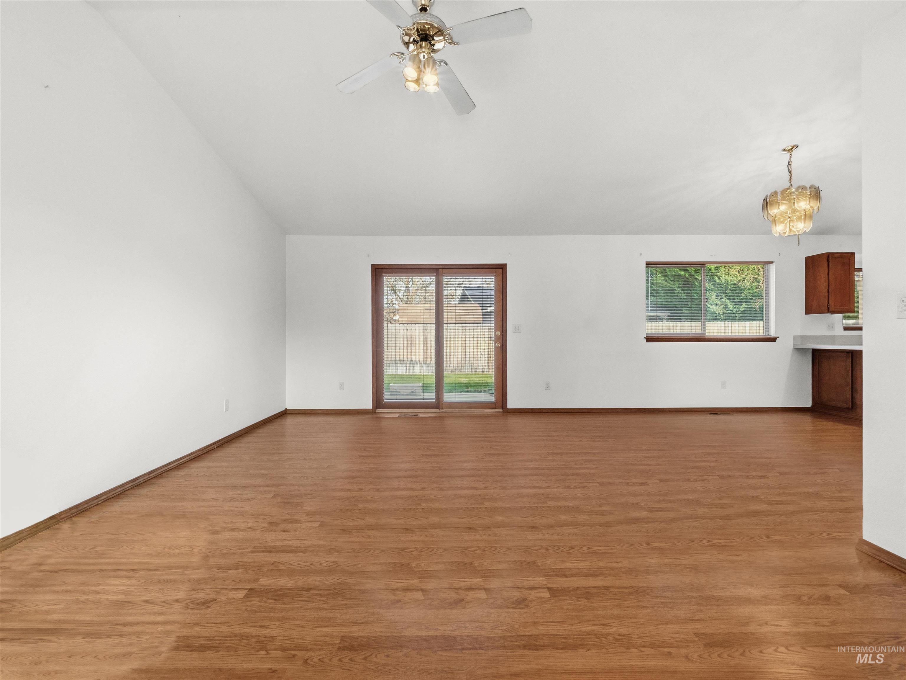 Unfurnished living room featuring plenty of natural light, light wood-style flooring, a chandelier, and vaulted ceiling