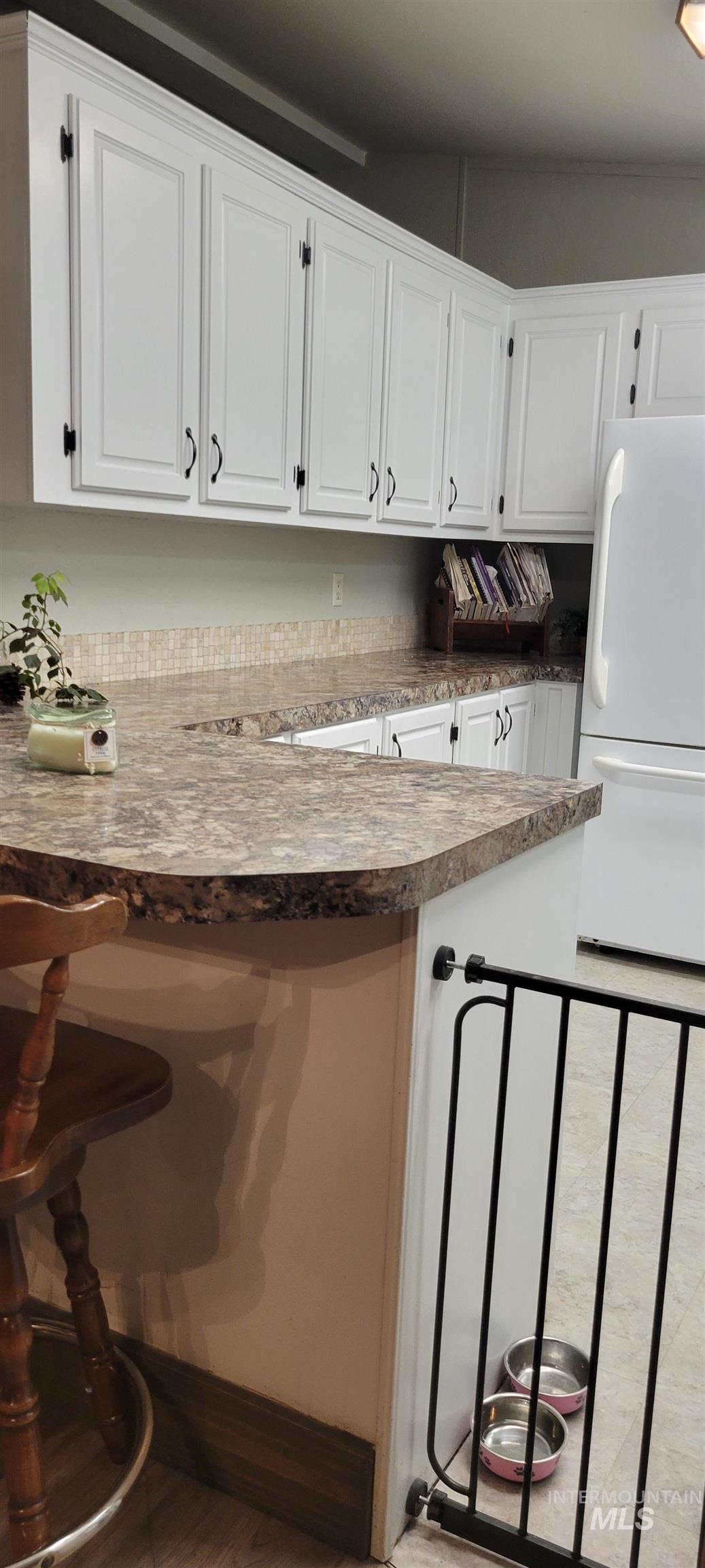 Kitchen featuring a breakfast bar area, white cabinets, freestanding refrigerator, and a peninsula