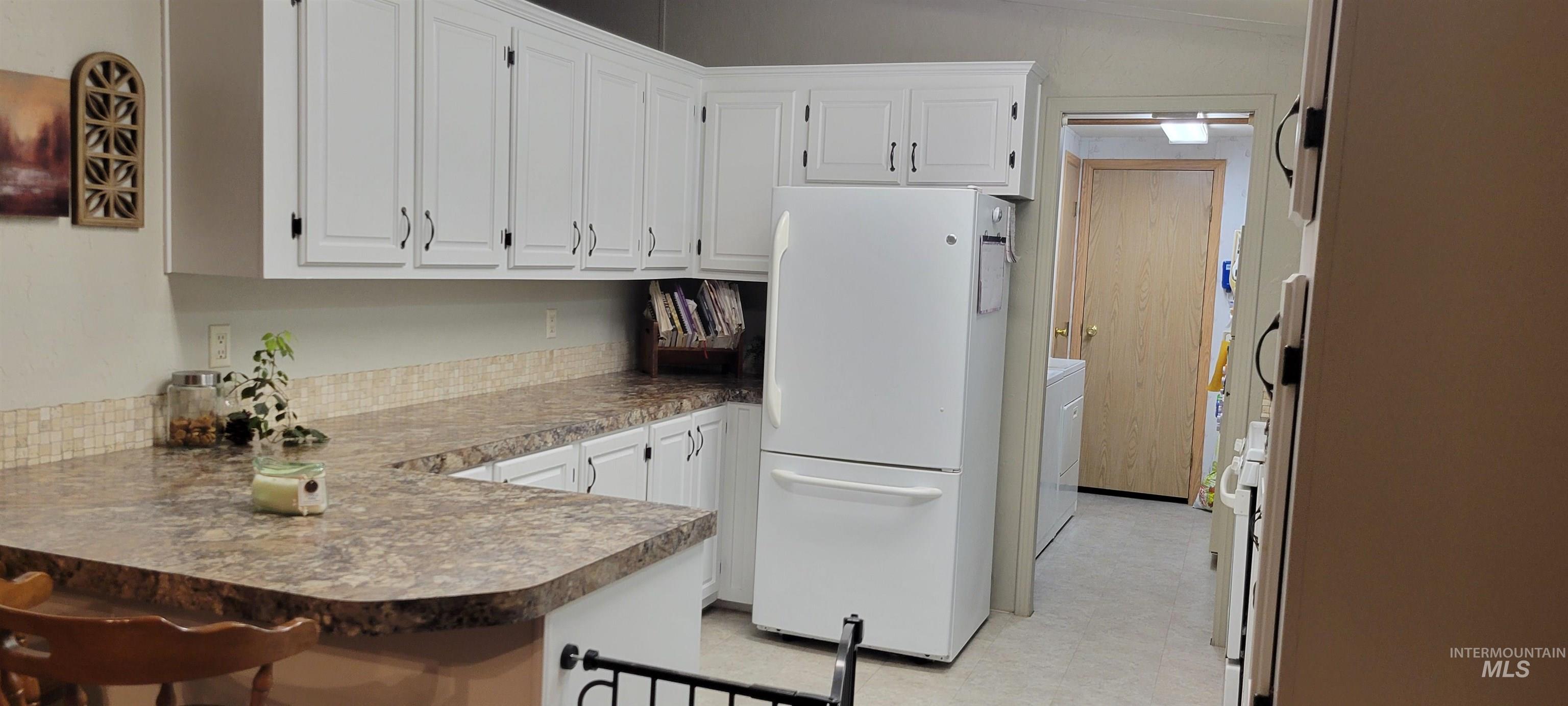 Kitchen featuring freestanding refrigerator, white cabinetry, a peninsula, and a kitchen bar