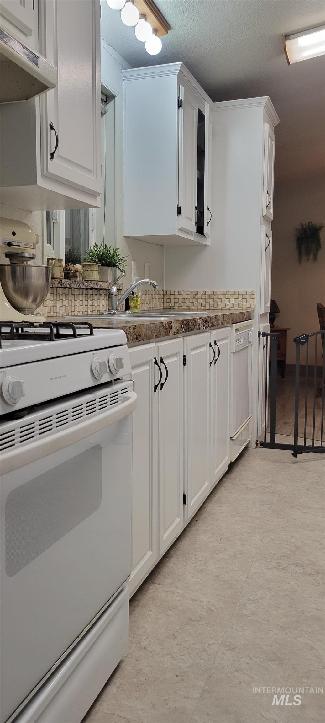 Kitchen featuring white gas stove, white cabinets, a textured ceiling, under cabinet range hood, and glass insert cabinets
