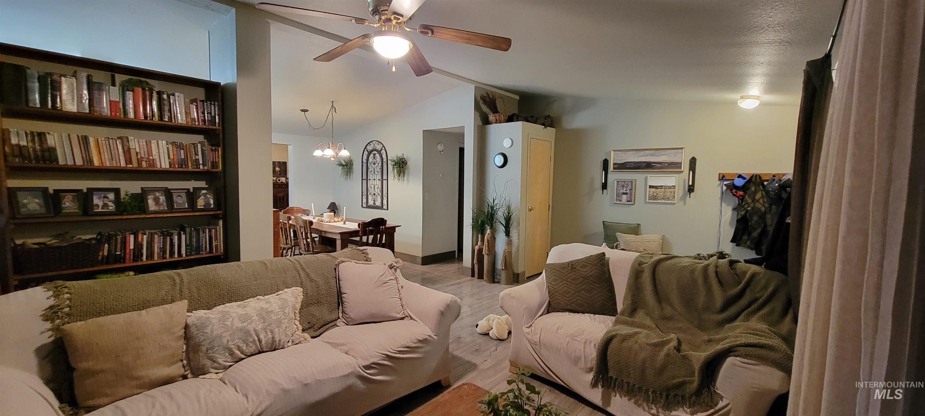 Living room featuring vaulted ceiling, a ceiling fan, a chandelier, and wood finished floors