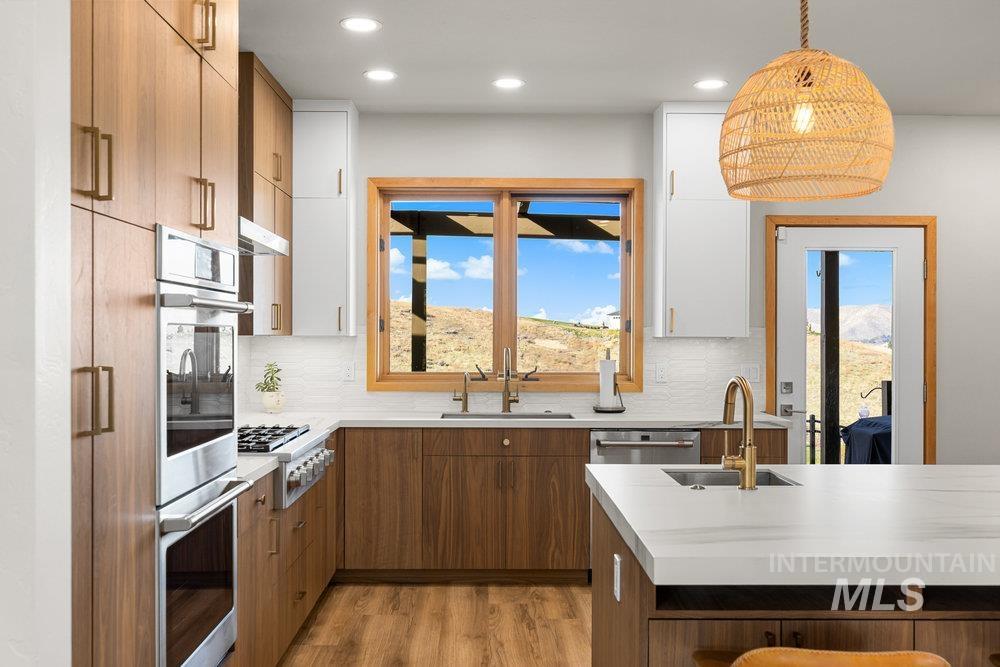 Kitchen with appliances with stainless steel finishes, brown cabinets, light wood-type flooring, recessed lighting, and hanging light fixtures
