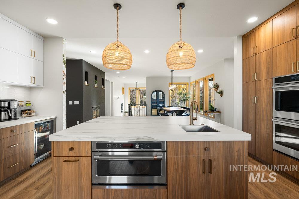 Kitchen with decorative light fixtures, brown cabinets, dark wood-style flooring, modern cabinets, and a center island with sink