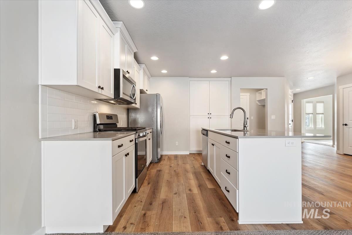 Kitchen with appliances with stainless steel finishes, white cabinetry, a kitchen island with sink, tasteful backsplash, and recessed lighting