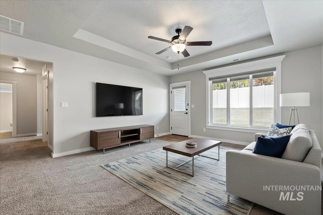 Living room with a raised ceiling, carpet floors, ceiling fan, and a textured ceiling