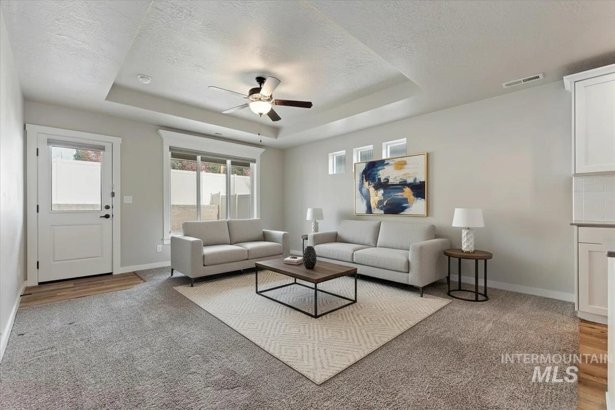 Living area featuring a raised ceiling, ceiling fan, and light carpet