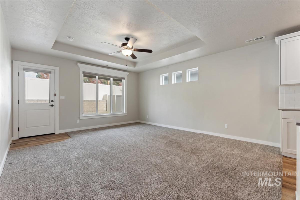 Unfurnished living room featuring a tray ceiling, a ceiling fan, light carpet, and a textured ceiling