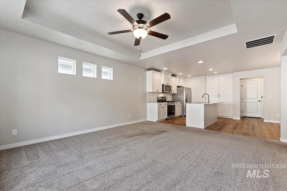 Unfurnished living room featuring a raised ceiling, light carpet, a ceiling fan, and recessed lighting