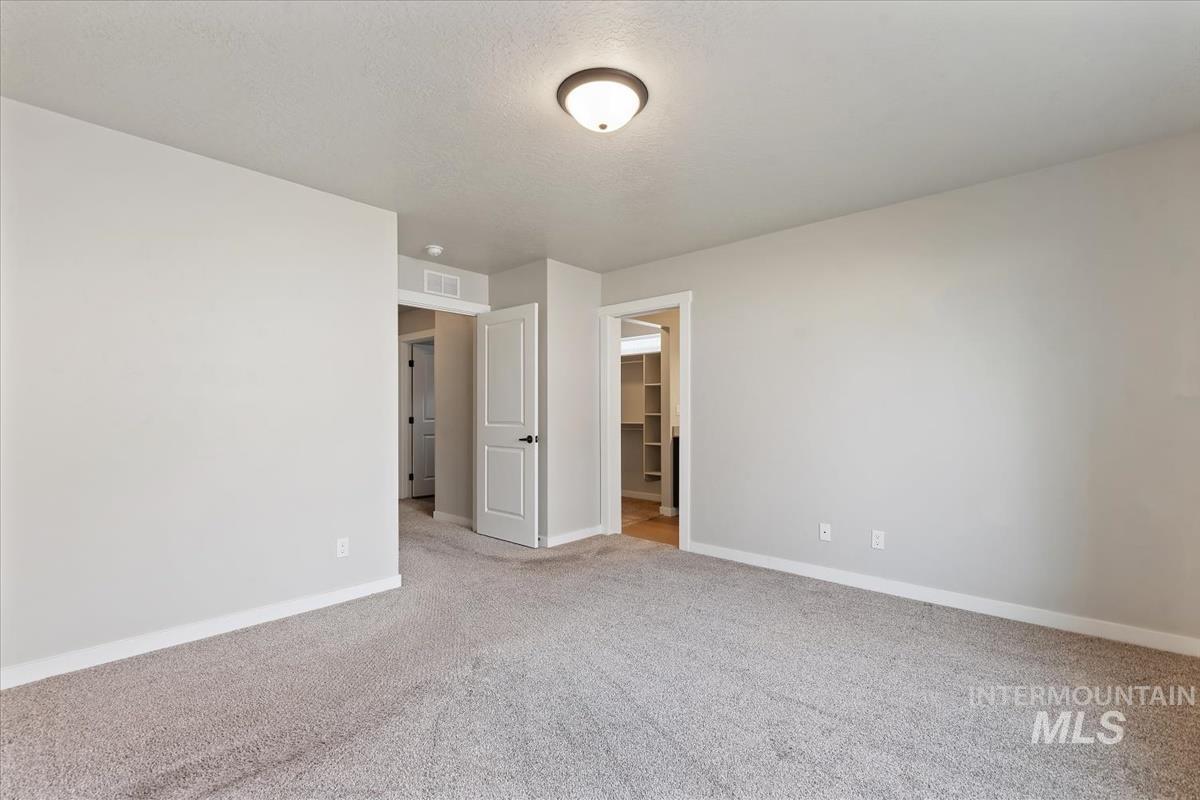 Unfurnished bedroom with carpet floors, a walk in closet, and a textured ceiling