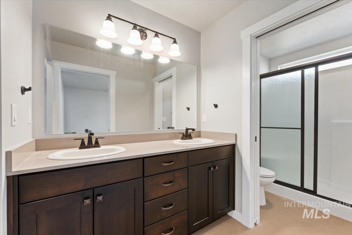 Full bath with double vanity, a shower stall, and light colored carpet