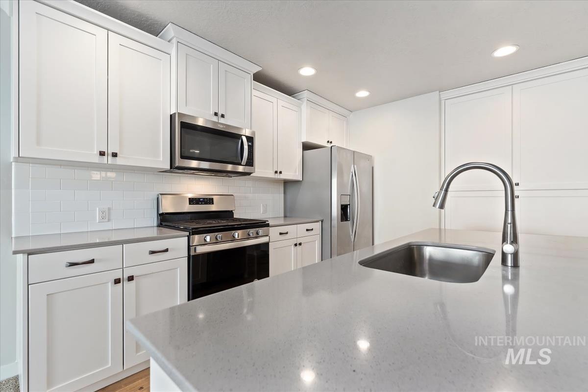 Kitchen with stainless steel appliances, white cabinetry, recessed lighting, light stone counters, and backsplash