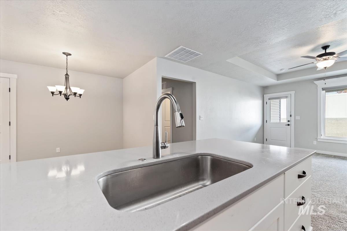 Kitchen featuring light colored carpet, white cabinetry, light stone counters, a textured ceiling, and pendant lighting