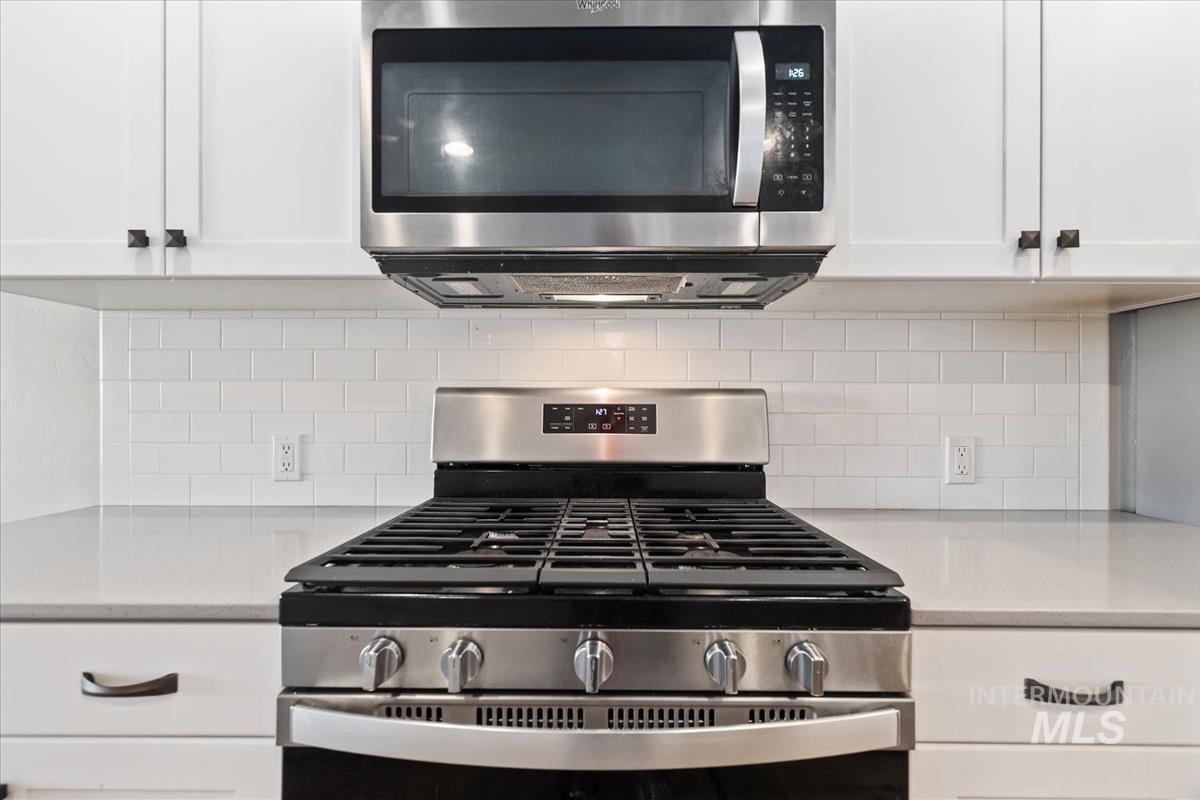 Kitchen with stainless steel appliances, white cabinetry, light stone countertops, and tasteful backsplash