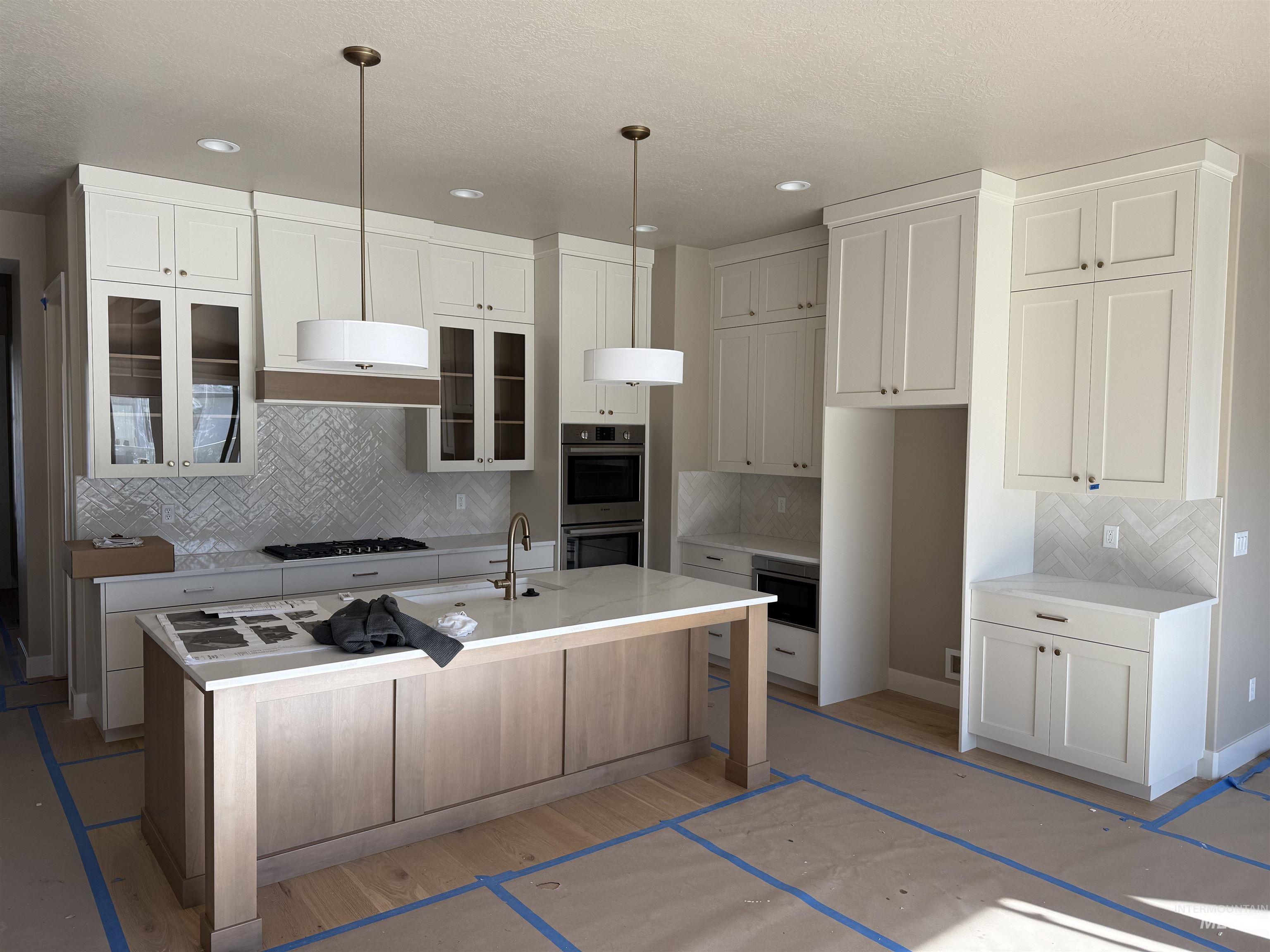 Kitchen with tasteful backsplash, a center island with sink, white cabinets, appliances with stainless steel finishes, and pendant lighting