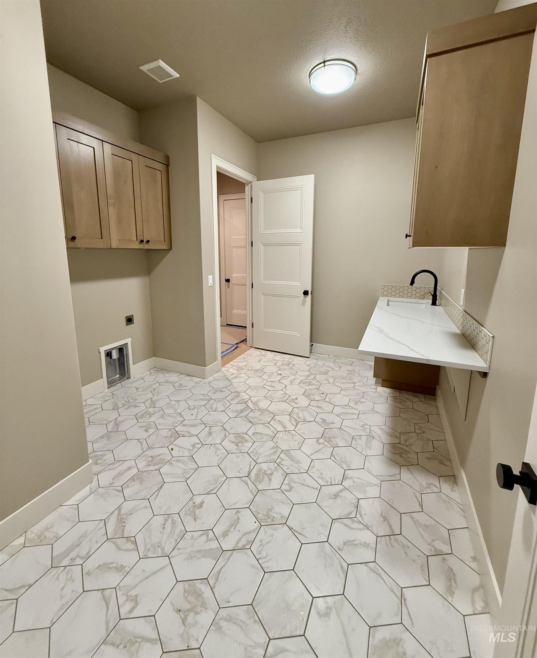 Laundry room with hookup for an electric dryer, cabinet space, and a textured ceiling